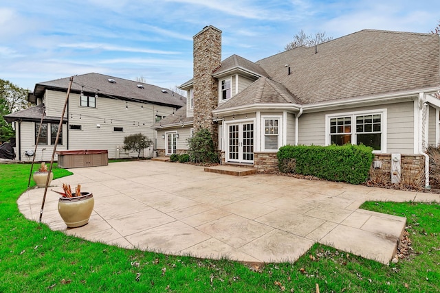 back of property with a chimney, a patio area, french doors, stone siding, and a hot tub