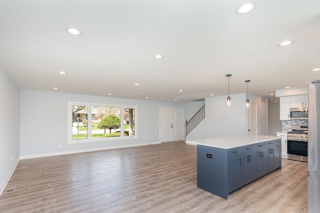 kitchen with open floor plan, light wood-type flooring, light countertops, appliances with stainless steel finishes, and a kitchen island