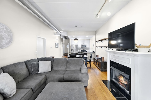 living room featuring light wood-style floors, a fireplace with flush hearth, and rail lighting