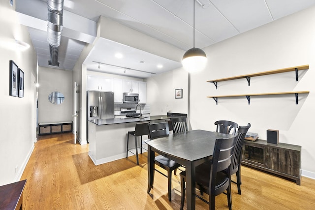 dining room featuring light wood-style flooring, rail lighting, and baseboards