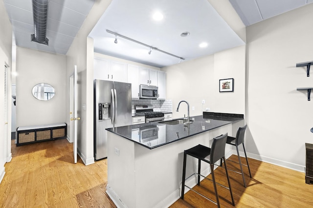 kitchen with stainless steel appliances, a sink, a peninsula, white cabinets, and a breakfast bar area