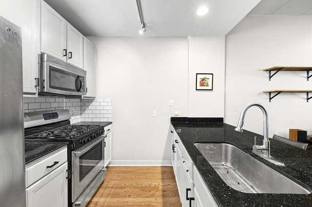 kitchen featuring stainless steel appliances, a sink, dark stone counters, tasteful backsplash, and light wood finished floors