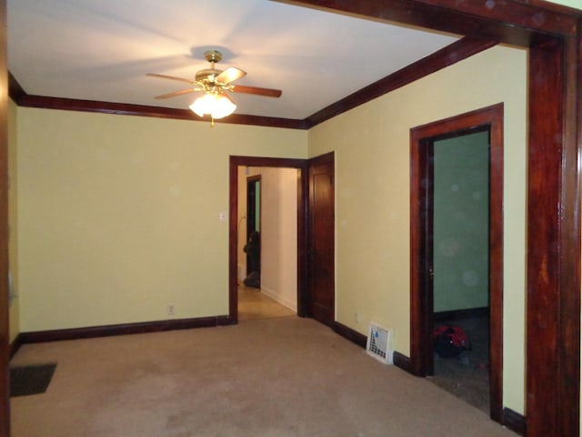 carpeted empty room featuring visible vents, ornamental molding, baseboards, and ceiling fan
