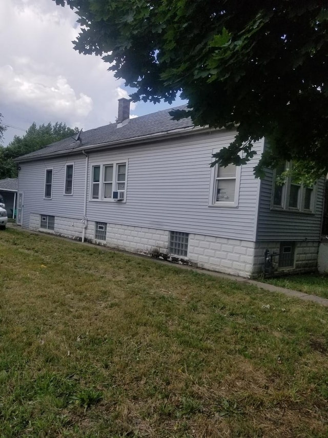 view of side of home with a shingled roof, a chimney, a yard, and cooling unit