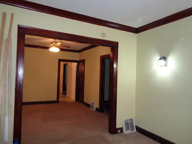hallway with carpet floors, visible vents, crown molding, and baseboards