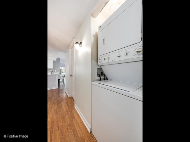 laundry room featuring baseboards, stacked washer and dryer, laundry area, and light wood-style flooring