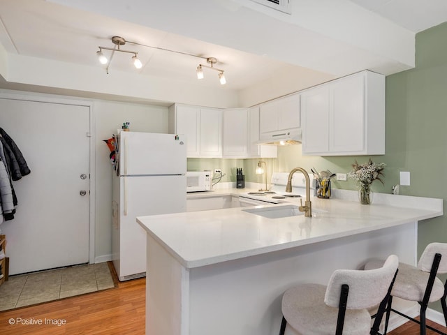 kitchen with light wood finished floors, a peninsula, white appliances, light countertops, and under cabinet range hood