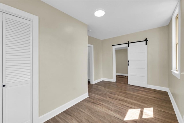 unfurnished bedroom featuring baseboards, a barn door, wood finished floors, and a closet