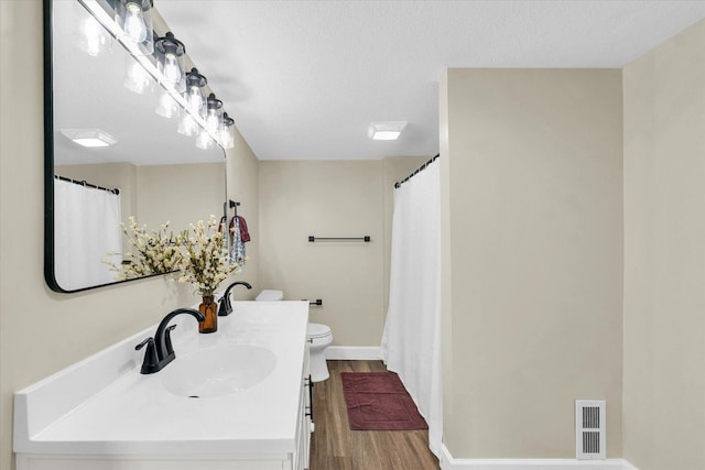 full bathroom featuring visible vents, vanity, wood finished floors, toilet, and a textured ceiling