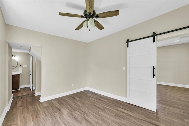unfurnished room featuring baseboards, ceiling fan, a barn door, and wood finished floors