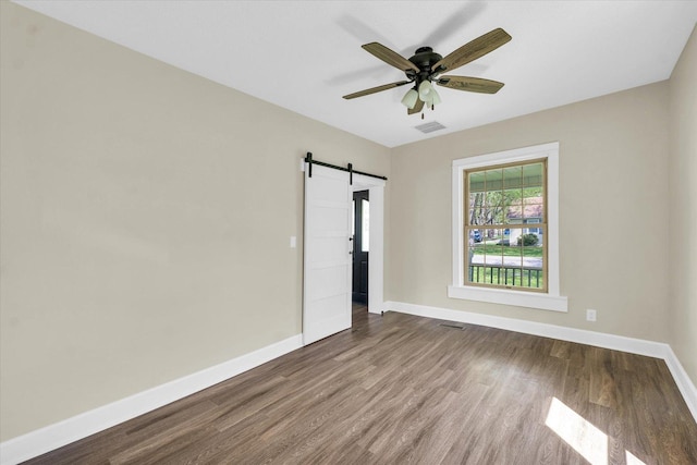 unfurnished room with visible vents, wood finished floors, baseboards, ceiling fan, and a barn door
