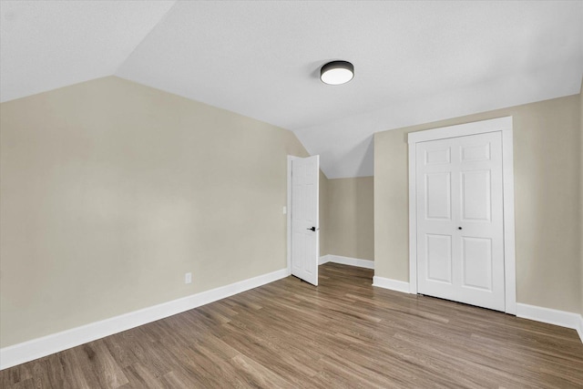 additional living space featuring baseboards, wood finished floors, and vaulted ceiling