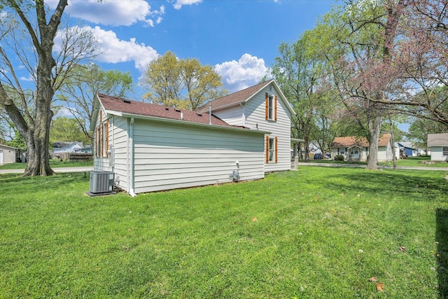 view of side of property featuring central air condition unit, a yard, and roof with shingles