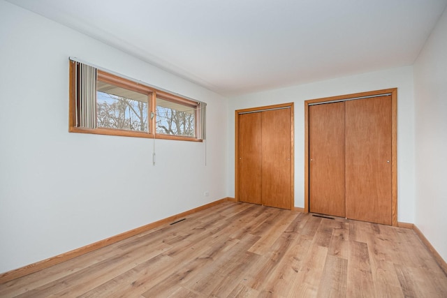 unfurnished bedroom featuring light wood-style floors, multiple closets, baseboards, and visible vents
