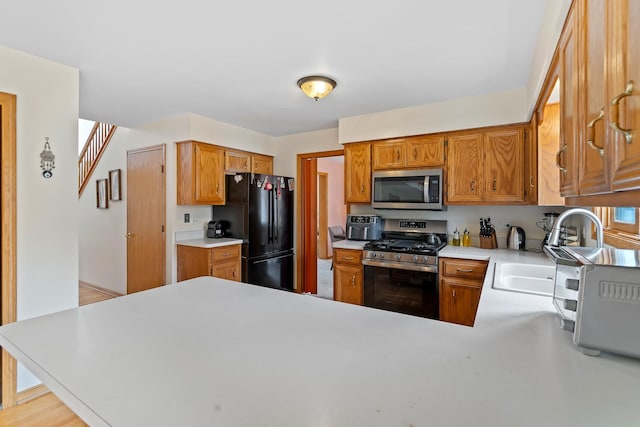 kitchen featuring stainless steel appliances, light countertops, a sink, a peninsula, and brown cabinetry