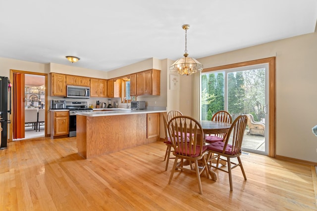 kitchen featuring stainless steel appliances, a peninsula, light wood-type flooring, a chandelier, and brown cabinetry