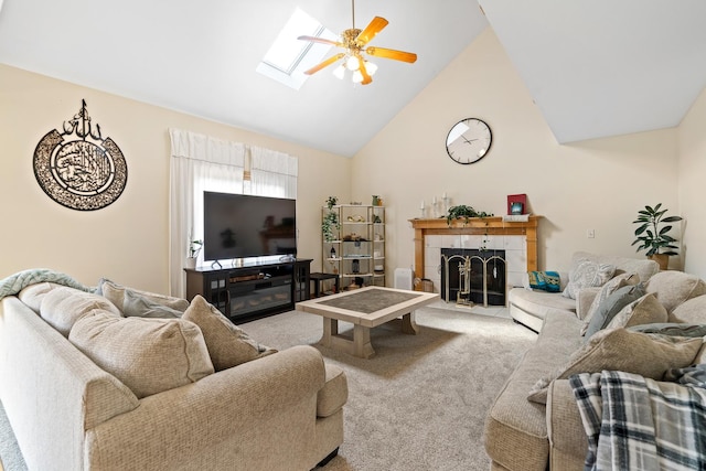 carpeted living area with high vaulted ceiling, a ceiling fan, a skylight, and a tiled fireplace