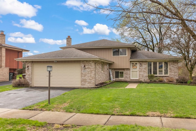 split level home featuring a chimney, a front yard, brick siding, aphalt driveway, and an attached garage