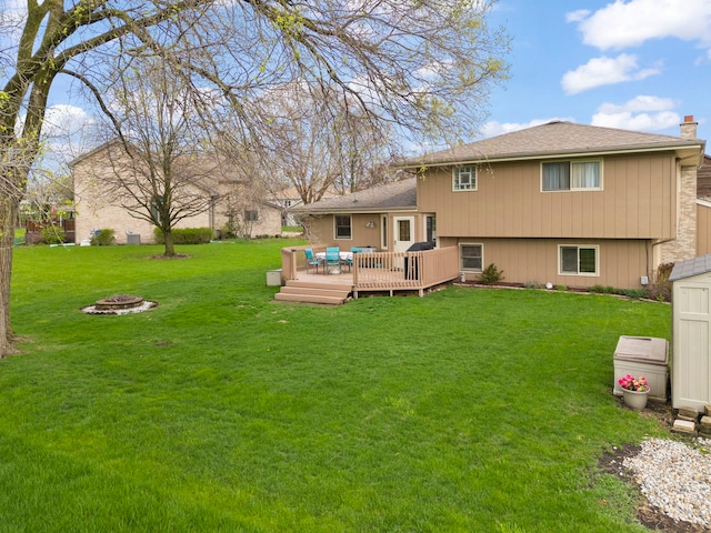 back of house featuring a lawn, a fire pit, a wooden deck, and a chimney