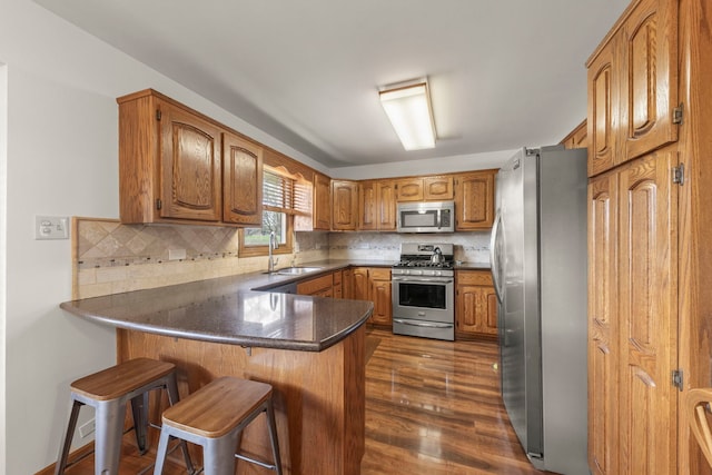 kitchen with a sink, brown cabinetry, stainless steel appliances, a peninsula, and decorative backsplash