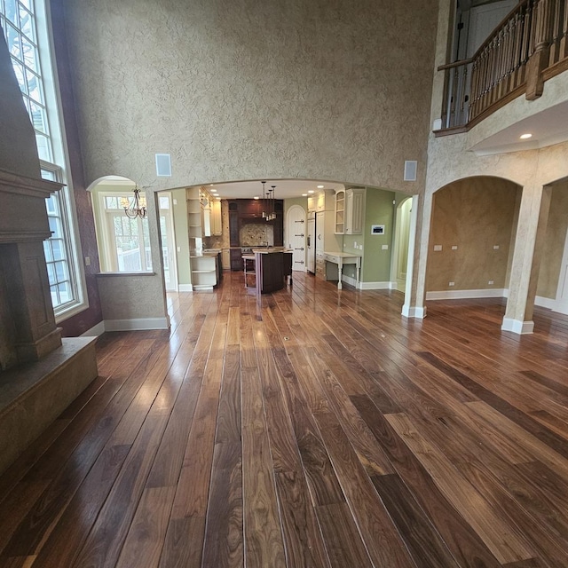 9065 Edinburgh Ct, Lakewood, IL 60014 - unfurnished living room with arched walkways, dark wood finished floors, baseboards, a chandelier, and a high ceiling