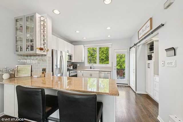 kitchen with appliances with stainless steel finishes, a sink, dark wood finished floors, a peninsula, and glass insert cabinets