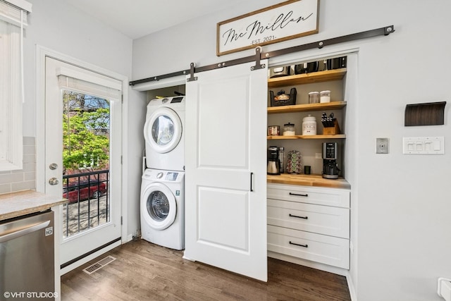clothes washing area featuring laundry area, visible vents, a barn door, stacked washing maching and dryer, and dark wood-style floors