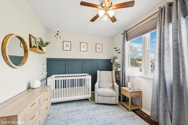 bedroom featuring visible vents, a decorative wall, wood finished floors, a nursery area, and a ceiling fan