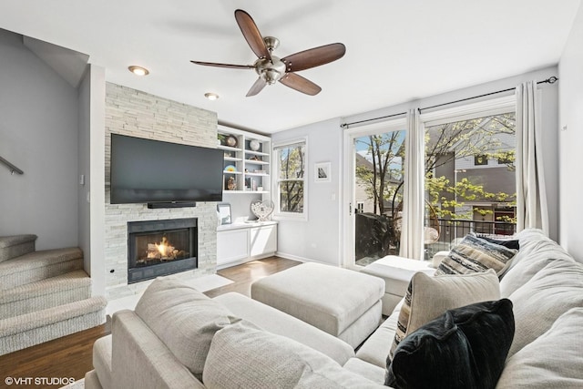 living area featuring stairs, wood finished floors, a fireplace, baseboards, and a ceiling fan