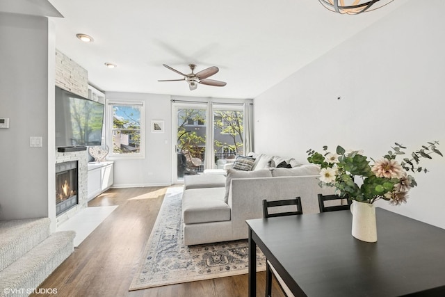 living area with baseboards, a fireplace with flush hearth, ceiling fan, and wood finished floors