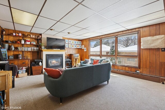 living room featuring a baseboard heating unit, a glass covered fireplace, carpet flooring, and wooden walls