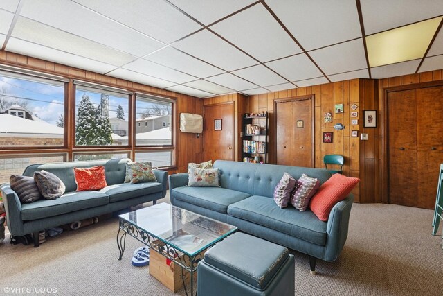 carpeted living area with wooden walls and a drop ceiling