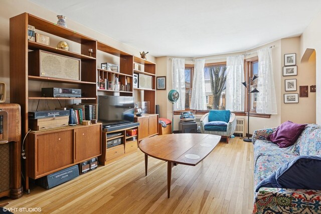 living area featuring radiator, light wood-type flooring, and arched walkways