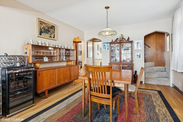 dining area featuring stairs, beverage cooler, arched walkways, and light wood-style floors