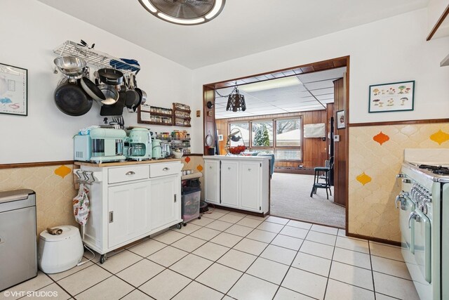 kitchen featuring a wainscoted wall, tile walls, white gas range oven, light colored carpet, and white cabinetry