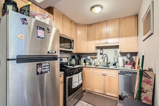 kitchen with a sink, light brown cabinetry, stainless steel appliances, and light stone counters