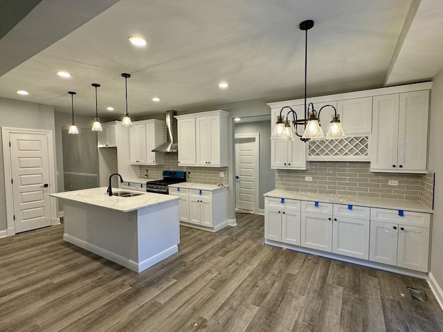 kitchen featuring wall chimney range hood, a sink, decorative backsplash, gas range, and white cabinetry