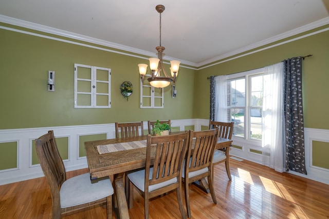 dining area featuring a chandelier, a decorative wall, light wood-type flooring, crown molding, and a wainscoted wall
