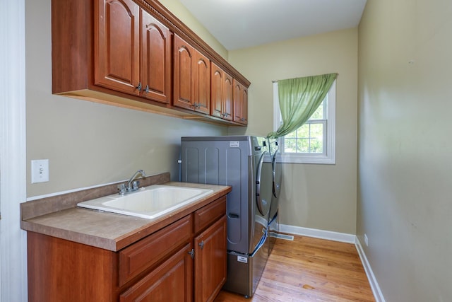 laundry area featuring washing machine and dryer, cabinet space, light wood finished floors, and baseboards