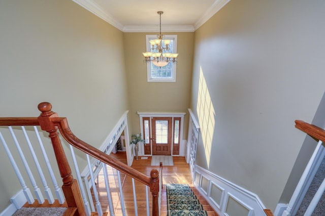 entryway with a chandelier, light wood-style floors, ornamental molding, stairway, and a towering ceiling