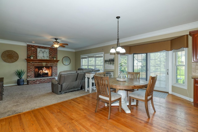 dining room with crown molding, light wood-style floors, a fireplace, a ceiling fan, and baseboards