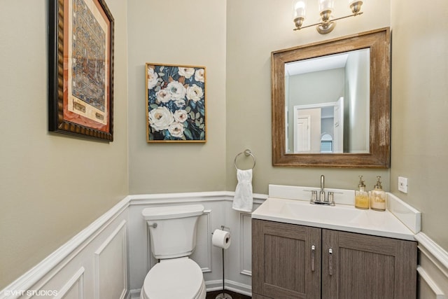 bathroom with vanity, a decorative wall, toilet, and a wainscoted wall