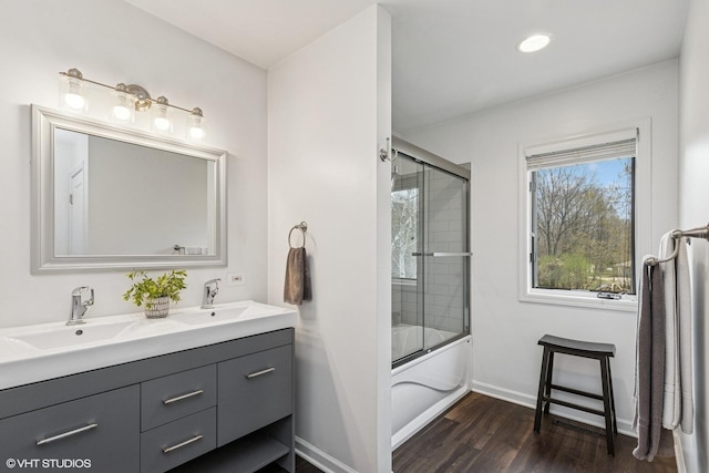 full bath with double vanity, a sink, wood finished floors, and shower / bath combination with glass door