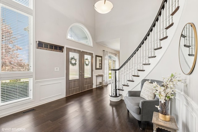 foyer entrance with a high ceiling, wainscoting, french doors, stairs, and dark wood-type flooring