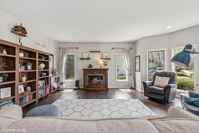 living area featuring a glass covered fireplace, baseboards, dark wood-style floors, and visible vents