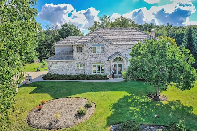 view of front of home featuring a high end roof, a chimney, a front lawn, and brick siding