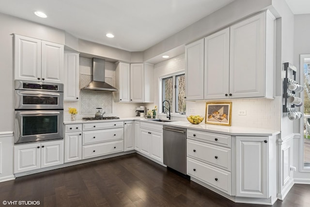 kitchen with a sink, wall chimney exhaust hood, appliances with stainless steel finishes, and light countertops