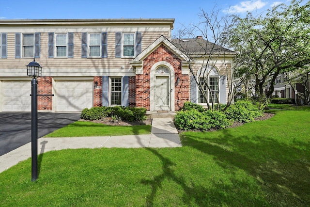 view of front of home featuring brick siding, a garage, a front yard, a chimney, and driveway