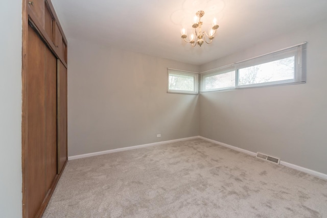 unfurnished bedroom featuring baseboards, visible vents, a notable chandelier, light colored carpet, and a closet