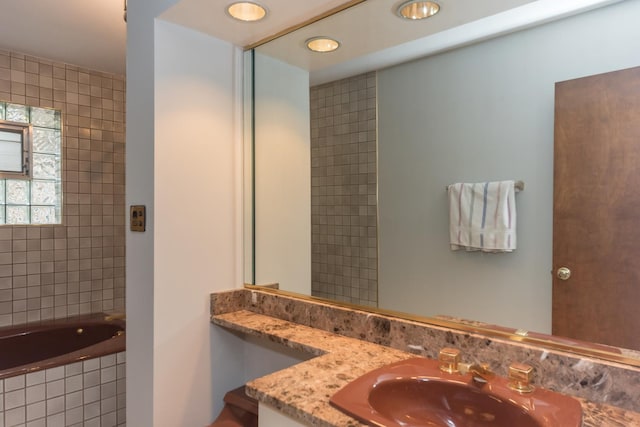bathroom featuring tiled tub, vanity, and recessed lighting